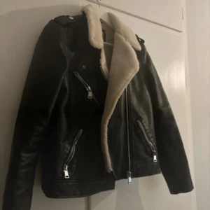 Svart skinnjacka med foder - Säljer en svart skinnjacka från ”pimkie” med mysigt vitt foder. Jackan har dragkedjor och en klassisk bikerstil. Perfekt för kyligare dagar. Fint skick, endast lite slitningar på ärmarna. 🙂