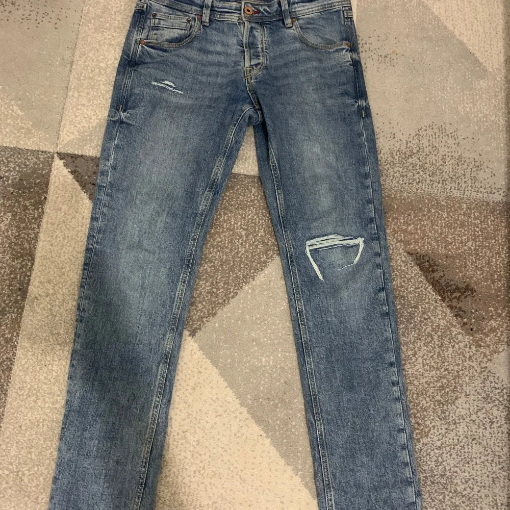Snygga blå jeans från Jack & Jones med slitna detaljer. De har en klassisk femficksdesign och en knappgylf. Perfekta för en avslappnad stil.. Farkut & Housut.
