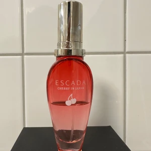 Escada Cherry in Japan Parfym - Säljer en elegant parfymflaska från Escada med doften 'Cherry in Japan'. Flaskan är röd och har en stilren design med ett silverfärgat lock. Perfekt för den som älskar fruktiga och blommiga dofter. 🍒