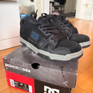 Svarta sneakers från DC Shoes - Säljer ett par svarta sneakers från DC Shoes med grå och blå detaljer. Skorna har en robust design med snörning och en bekväm sula. Perfekta för en avslappnad stil.