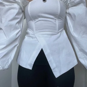 Elegant vit blus med puffärmar - Elegant vit blus med puffiga långa ärmar och en unik asymmetrisk nederdel. Ditsydd knapp . 