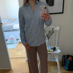 Ljusblå skjorta - Säljer en stilren ljusblå skjorta med klassisk krage och knappar framtill. Skjortan har långa ärmar och en figursydd passform. Passar bra till både jeans och kostymbyxor. OBS - inte struken på bilderna!
