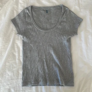 Grå ribbad topp från Brandy Melville - Säljer en grå ribbad topp från Brandy Melville. Toppen har en rund halsringning och korta ärmar, perfekt för en avslappnad look. Den är i en mjuk och bekväm bomullsblandning. Skulle passa någon som har storlek S eller XS. Har inte använt mycket alls då den är lite för liten för mig.💗