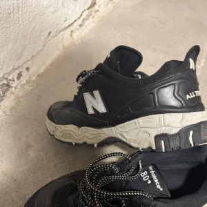 Svarta New Balance sneakers - Säljer ett par svarta New Balance sneakers med vit sula och klassisk snörning. Skorna har en robust design med märkets logga på sidan och undersidan. Perfekta för en aktiv livsstil.