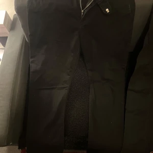 Svarta byxor med dragkedja - Snygga svarta byxor med dragkedja framtill. Perfekta för en stilren look. Passar bra till både vardag och mer uppklädda tillfällen.