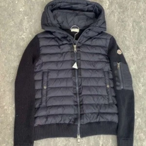 Moncler cardigan  - Snygg mörkblå jacka från Moncler med quiltad design och stickade ärmar. Jackan har en praktisk huva och dragkedja framtill. Perfekt för kyligare dagar med sin stilrena look och funktionella fickor. OBS KOMMER UTAN KVITTO!! Passar s/m