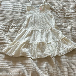 Vit klänning med volanger - Säljer en söt vit klänning med smala axelband och flera lager av volanger. Perfekt för varma sommardagar. Klänningen har en luftig och bekväm passform. Köpte den på rea så säljer endast för 120kr ordinarie pris: 400kr