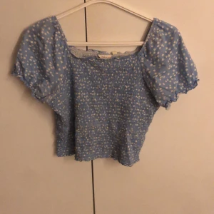 Blå blommig topp - Söt blå topp med vita prickar och korta puffärmar. Den har en smockad design som ger en fin passform och är croppad i modellen. Perfekt för en somrig look! Den är i storlek 170 men skulle säga att den passar s-m❤️❤️