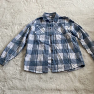 Blå och vit rutig skjorta - Säljer en stilren blå och vit rutig skjorta med långa ärmar och knappar framtill. Skjortan har två bröstfickor , perfekt för en avslappnad look. Passar bra till både jeans och chinos. 🌀