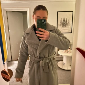 Grå kappa med bälte - Säljer en  grå kappa med bälte. Den har använts eb del men är i bra skick! 