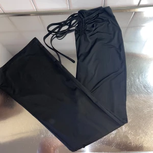 Svarta byxor med snörning - Snygga svarta byxor med snörning i midjan. De har en tight passform och är tillverkade i ett mjukt syntetmaterial. Perfekta för en stilren look.