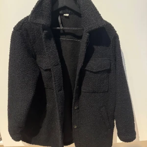 Svart teddyjacka med knappar - teddyjacka med knappar framtill och två stora fickor på bröstet. fint skick, den är använt fåtal gånger