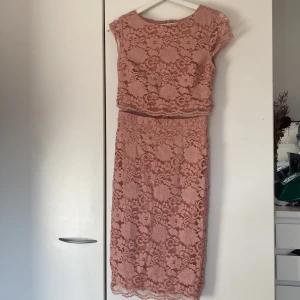 Rosa spetsklänning från NLY EVE - Säljer en fin rosa spetsklänning från NLY EVE. Klänningen har korta ärmar och en vacker blommig spetsdesign. Den ser ut som att den  tvådelad med en topp och en kjol, men den sitter ihop med genomskinligt tyg, vilket ger en fin look. Perfekt för speciella tillfällen! 🌸