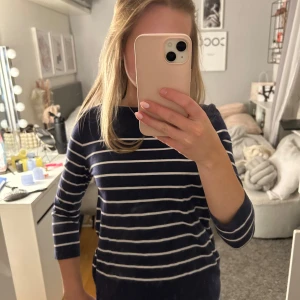 Mörkblå randig tröja - Säljer en snygg mörkblå tröja med vita ränder. Tröjan har trekvartsärmar och en klassisk design som passar perfekt till vardags. Perfekt för dig som gillar en stilren look!