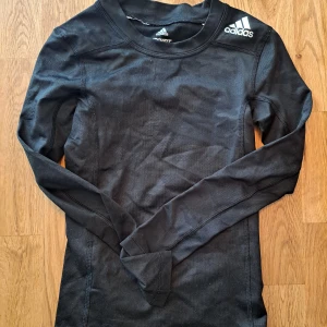 Svart långärmad tröja från Adidas - Säljer en svart långärmad tröja från Adidas med Techfit och ClimaWarm-teknologi. Perfekt för träning och håller dig varm. Adidas-logga på axeln ger en sportig look.