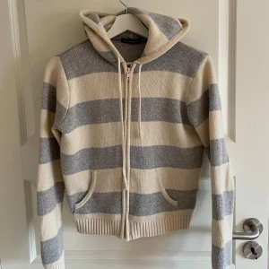 Randig hoodie från Brandy Melville - Säljer en mysig randig hoodie från Brandy Melville i beige och grått. Tröjan har dragkedja framtill och en praktisk huva. 🤍