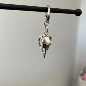 Silverfärgat örhänge i rostfritt stål med fågelkranium - Unikt silverfärgat örhänge format som ett fågelkranium. Perfekt för att ge en edgy touch till din stil. Lätt och bekvämt att bära.