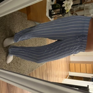 Blå randiga pyjamasbyxor med snörning - Säljer ett par bekväma blå byxor med vita ränder. De har en avslappnad passform och snörning i midjan för justerbarhet. Perfekta för en avslappnad dag hemma eller ute.