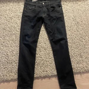 Replay jeans - Snygga svarta jeans från Replay, modell Anbass. De har en klassisk femficksdesign med guldfärgade nitar och en knappgylf. Perfekta för en stilren look. Storlek 34/32 har haft dem 3-4 gånger 