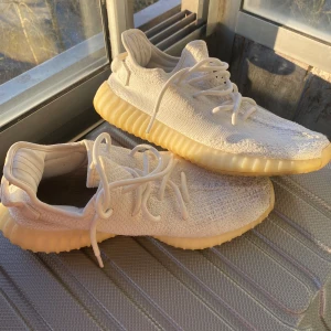 Vita Adidas Yeezy sneakers - Säljer ett par vita Adidas Yeezy sneakers med en unik design och bekväm passform. Skorna har en stickad ovandel och en karakteristisk ribbad sula i beige. Perfekta för en stilren look.