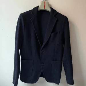 Mörkblå kavaj - Snygg stickad italiensk kavaj från Forpen med ett diskret rutmönster. I nyskick, inga hål eller liknande. Perfekt för alla tillfällen. Storlek: Small (44). Priset är inte hugget i sten! 