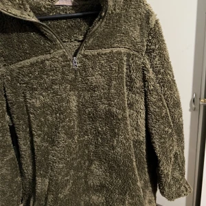 Olivgrön fleece tröja med dragkedja - Mysig olivgrön fleece tröja med halv dragkedja. Perfekt för kyliga dagar med sin mjuka och fluffiga textur. Tröjan har långa ärmar och en hög krage för extra värme.