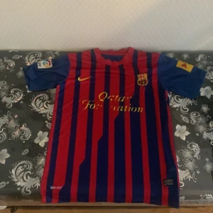 Blå PSG fotbollströja och Barca tröja  - Säljer en blå PSG fotbollströja med korta ärmar och snygga vita och röda detaljer vid krage och ärmslut. Tröjan har nummer 30 på ryggen och sponsorloggor på framsidan. Perfekt för fotbollsfans som vill visa sitt stöd för laget!