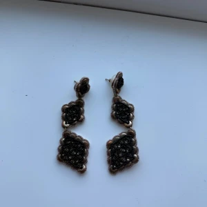 Svarta glittriga örhängen - Eleganta svarta örhängen med glittrig yta och fyrkantig design. De har en hängande stil med två sammanlänkade delar, vilket ger en sofistikerad look. Perfekta för att lägga till lite glamour till din outfit.