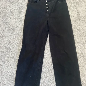 Svarta Ribcage Straight jeans, Levi’s - Säljer ett par svarta Ribcage Straight jeans från Levi's. De har en hög midja och knappar framtill. Klassisk design med fem fickor och en rak passform. Perfekta för en stilren look. 