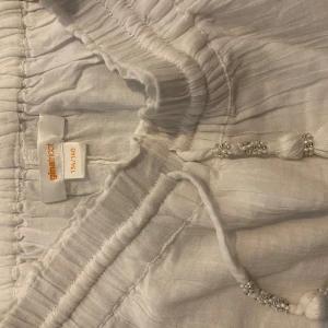 Volang kjol  - Vit volangkjol med fina detaljer på snörena. Passar till vardags och fest. Jag köpte liten strl så jag kunde ha den lågmidjad men andvände aldrig den. Helt ny. 