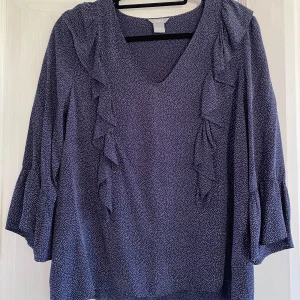 Söt blus säljes - Söt blus med volanger, tyget är marinblått med små vita prickar. Superfina vida trekvartsärmar. Snygg till jeans! Mycket gott skick, knappt använd. 