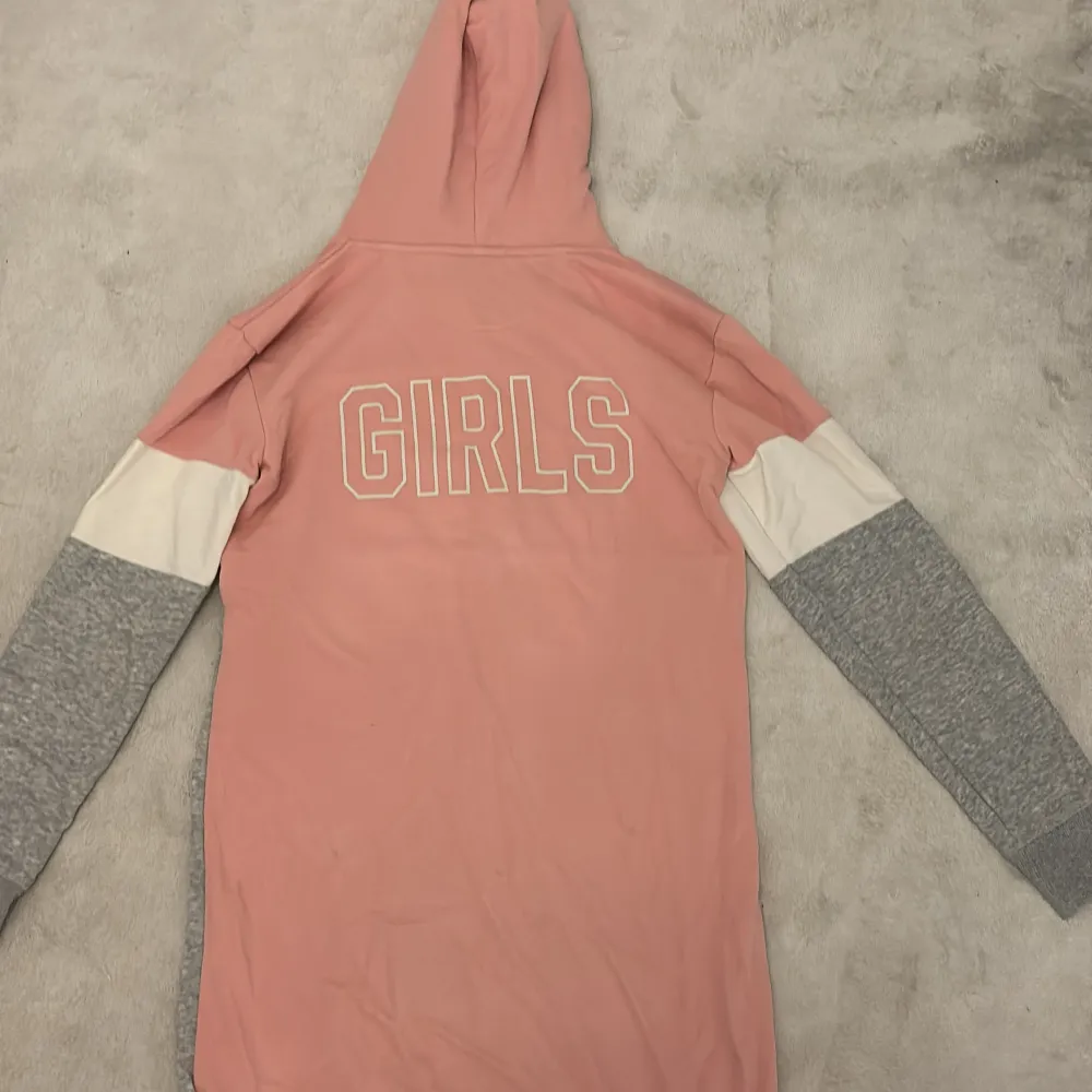 Jag säljer en superfin hoodie från GANT i rosa och grått med vit detalj. Den har en stor GANT-logga på framsidan och 'GIRLS' på baksidan. Perfekt för en avslappnad stil och mysiga dagar. Hoodien har långa ärmar och är gjord i mjukt material.. Hoodies.