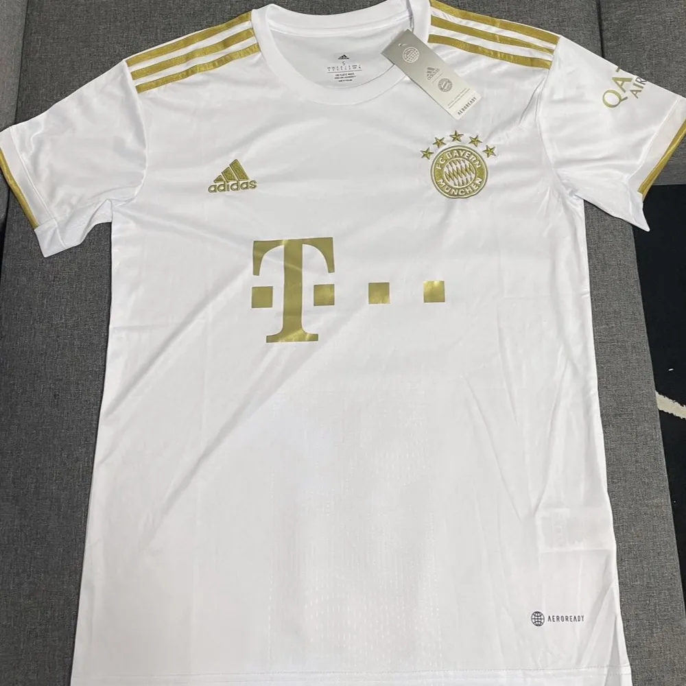 Säljer en snygg vit fotbollströja från Adidas med guldiga detaljer. Tröjan har korta ärmar och är i nyskick. Perfekt för fotbollsfans som vill ha en stilren look på planen eller till vardags.finns även i m. T-shirts.