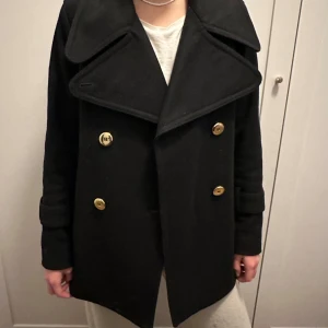 Svart skepparkavaj med guldknappar - Säljer denna yllejacka från Filippa K med guldknappar! Kan knäppas och bäras på olika sätt! Storlek XS men är större än så, är själv 170 cm lång! Ser ut som ny men innertyget lite upprivet på ena sidan! Bara att skriva för frågor!