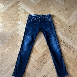 Mörkblå jeans från Replay - Säljer ett par snygga mörkblå jeans från Replay. De är i modellen Anbass och har en slim passform. Jeansen har en klassisk femficksdesign med dragkedja och knapp framtill. De är tillverkade i ett stretchigt material som ger en bekväm passform. 