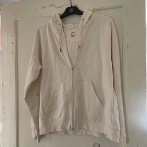 Beige hoodie i ekologisk bomull - Säljer en supermjuk och bekväm beige hoodie från märket C. Den är gjord av ekologisk bomull och har en dragkedja framtill. Perfekt för en avslappnad stil med sina långa ärmar och praktiska fickor. Passar perfekt för kyliga dagar!