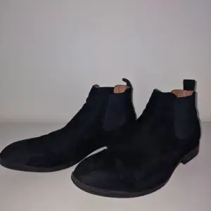 Säljer ett par stilrena svarta Chelsea boots i mocka. De har en klassisk design med elastiska paneler på sidorna för enkel på- och avtagning. Perfekta för både vardag och fest, och de ger en snygg touch till vilken outfit som helst. Använda men i bra skick!