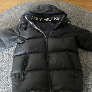 Säljer min Tommy hilfiger svart vinter jacka  - Denna jackan har blivt för liten det är bra skick väldigt varm under vintern storlek 164