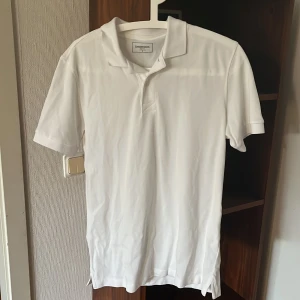 Vit pikétröja från Dressmann - Säljer en klassisk vit pikétröja från Dressmann i storlek S Perfekt för både vardag och lite mer uppklädda tillfällen. Tröjan har korta ärmar och en stilren krage med knappar. Materialet känns mjukt och bekvämt, perfekt för sommardagar. Passar bra ti