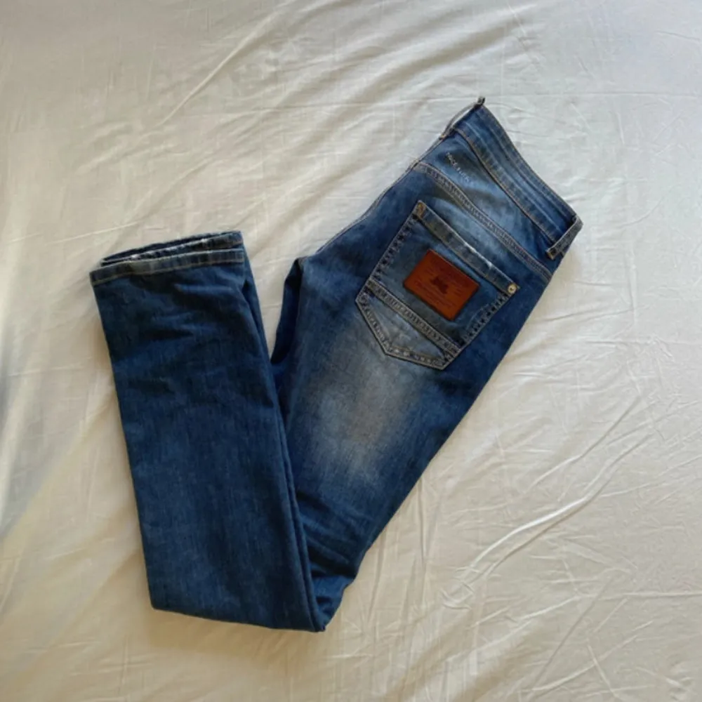 Säljer ett par snygga blå jeans från Dsquared2. De har en fet slitning och broderad logga på framsidan. Jeansen är tillverkade i Italien och har en klassisk femficksdesign. Perfekta för en avslappnad men stilren look! Nyskick! Storlek w28 l32.. Jeans & Byxor.