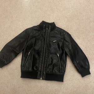 Svart skinnjacka från H&M - Säljer en cool svart skinnjacka från H&M i storlek EUR 92. Jackan har en dragkedja framtill och två fickor med dragkedjor. Perfekt för höst och vår, och ger en tuff look till vilken outfit som helst. Den är i bra skick och redo för nya äventyr!