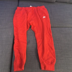 Röda mjukisbyxor från Nike - Säljer ett par röda mjukisbyxor från Nike i storlek XXL. Byxorna har en elastisk midja med snörning och är superbekväma för chill eller träning. De har en klassisk Nike-logga på ena benet och är gjorda i mjukt bomullsmaterial.