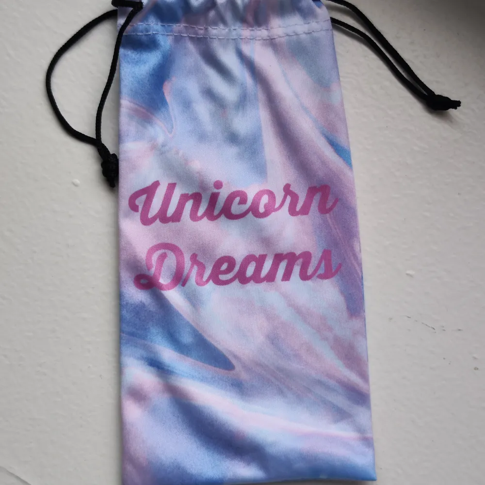 Ett supergulligt glasögonfodral med texten 'Unicorn Dreams' i rosa. Fodralet har ett drömlikt mönster i blått och lila, perfekt för att hålla dina glasögon säkra och stiliga.. Accessoarer.