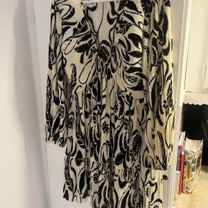 Svartvit mönstrad klänning - Säljer en elegant svartvit klänning med ett abstrakt mönster. Klänningen har långa ärmar och en v-ringad design som ger en stilren look. Perfekt för både vardag och festliga tillfällen. Materialet känns lätt och bekvämt mot huden.