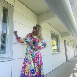 Färgglad blommig klänning - Säljer en superfin och färgglad blommig klänning med långa ärmar och en härlig mix av rosa, blå, gul och lila nyanser. Perfekt för sommarens fester eller en solig dag. Klänningen har en bekväm passform och är gjord i ett lätt och luftigt material. Den har en vacker lila kant längst ner som ger en extra touch. 🌸helt ny