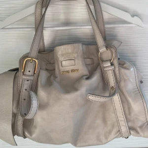 Miu Miu Väska - Säljer en beige/krämvit väska från Miu Miu. Perfekta presenten till modeälskaren!💞Väskan har justerbara remmar och en stilren design. Den har några fläckar och tecken på användning, men är fortfarande i bra skick. Slitage och färgfläckar förekommer. Köpt second hand men personligen aldrig använd. Kontakta för fler bilder. Blandning mellan bra och acceptabelt skick. Perfekt för vardagsbruk eller en dag på stan! 