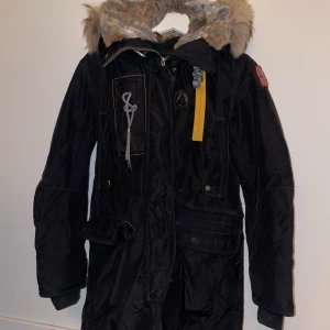 Svart vinterjacka från Parajumpers - Säljer min Parajumper kodiak vinterjacka i mycket bra skick. Jackan har en fluffig pälsfodrad huva och flera praktiska fickor. Jackan är i storlek xs, köpt från johnells använd 1 vinter. Säljer den då den bara legat i garderoben och dammat. Nypris 10.499kr. Muddarna på armarna är hela och fina, inga släpp. Inga andra skavanker på jackan. Kan skicka mer bilder för dig som är intresserad. Märket på högra armen är avtagsbar då man kan byta till en annan (svart märke), medföljer självklart.