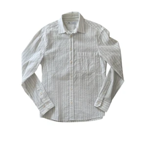 Vit och blå randig skjorta från Zara - Säljer en stilren vit skjorta med blå ränder från Zara. Skjortan har långa ärmar och knappar framtill. Perfekt för både vardag och fest! Tillverkad i ett lätt och bekvämt material.