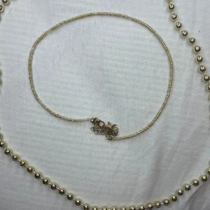 Guldhalsband med små pärlor - Snyggt och elegant guldhalsband med små pärlor. Perfekt för att ge en touch av glamour till vilken outfit som helst. Halsbandet har en fin låsdetalj som gör det enkelt att ta på och av. Passar både till vardags och festliga tillfällen.