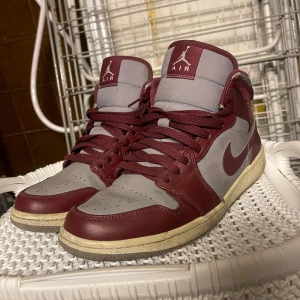 Air Jordan 1 MID Cherrywood Red - Säljer ett par snygga Nike Air Jordans i vinrött och grått. Skorna har klassisk snörning och en bekväm passform. Perfekta för både vardag och fest! De är i bra skick med en cool design som verkligen sticker ut. Modellen heter: Air Jordan 1 MID Cherrywood Red och dom kostar 2000kr ny pris på eBay och är storlek 42.